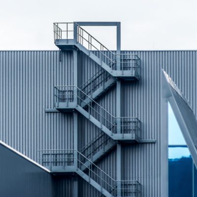 A gray metal wall with spiral stairs under the clear sky